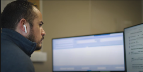 Builders’ General's employee sitting at his desk at Builders’ General Little Silver location. He is looking at two computer screens, there is an AirPod in his left ear.